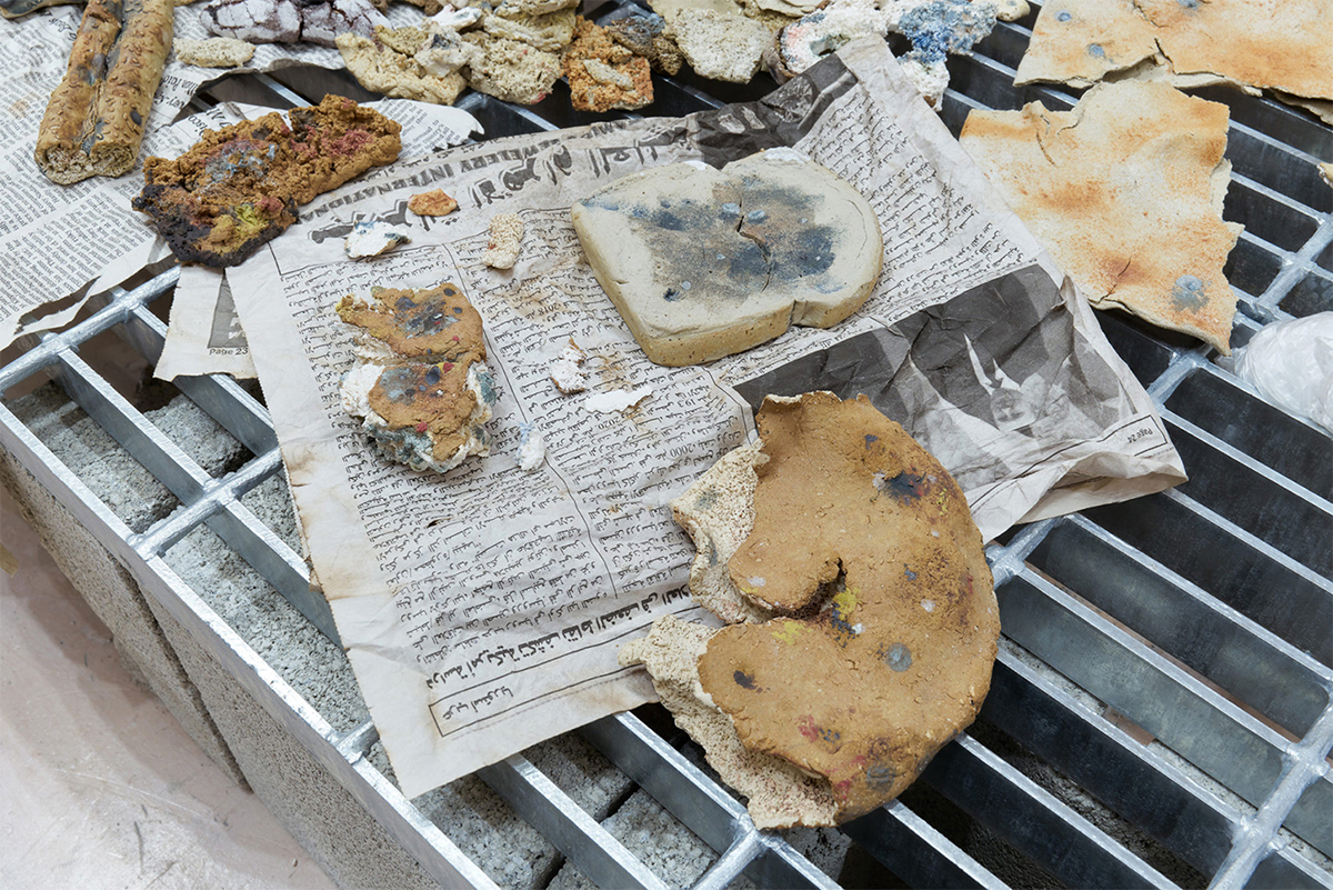 Closeup of sculpture showing stale and fragmented bread strewn across Arabic text newspapers.